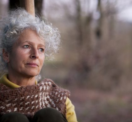 Portrait of grey haired mature woman gazing in woodland at dusk